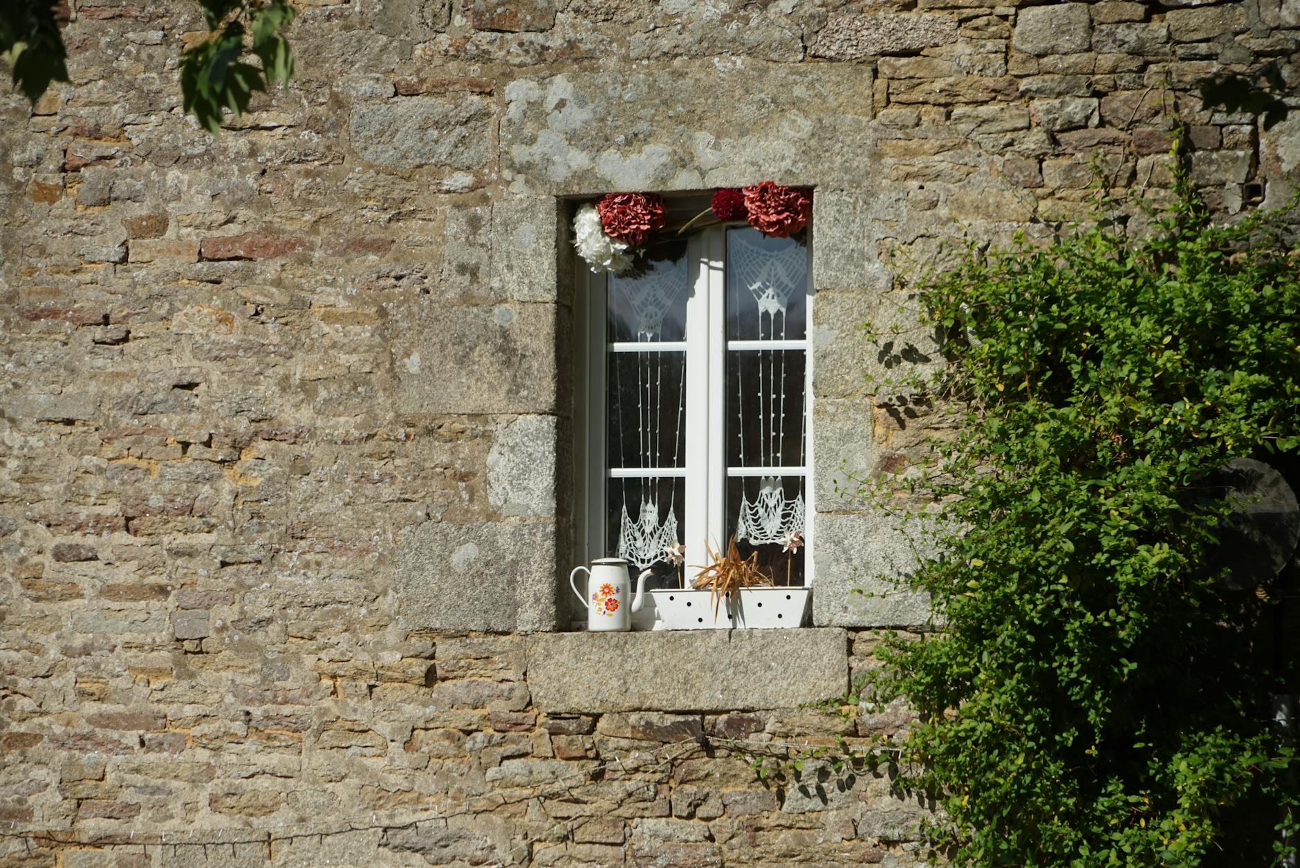 Kamienne okno domu z parapetem, białymi zasłonami i doniczkami z roślinami